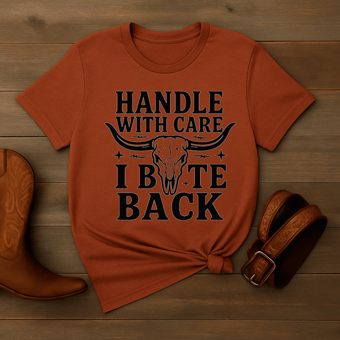 Orange t-shirt with graphic design and text on a wooden surface with cowboy boot and belt.