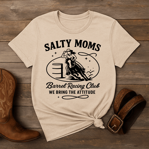 Beige t-shirt with 'Salty Moms Barrel Racing Club' graphic on a wooden surface with cowboy boots and a belt.