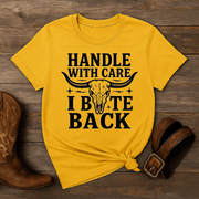Yellow t-shirt with a skull graphic and text on a wooden surface with cowboy boots and a belt.