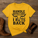 Yellow t-shirt with a skull graphic and text on a wooden surface with cowboy boots and a belt.