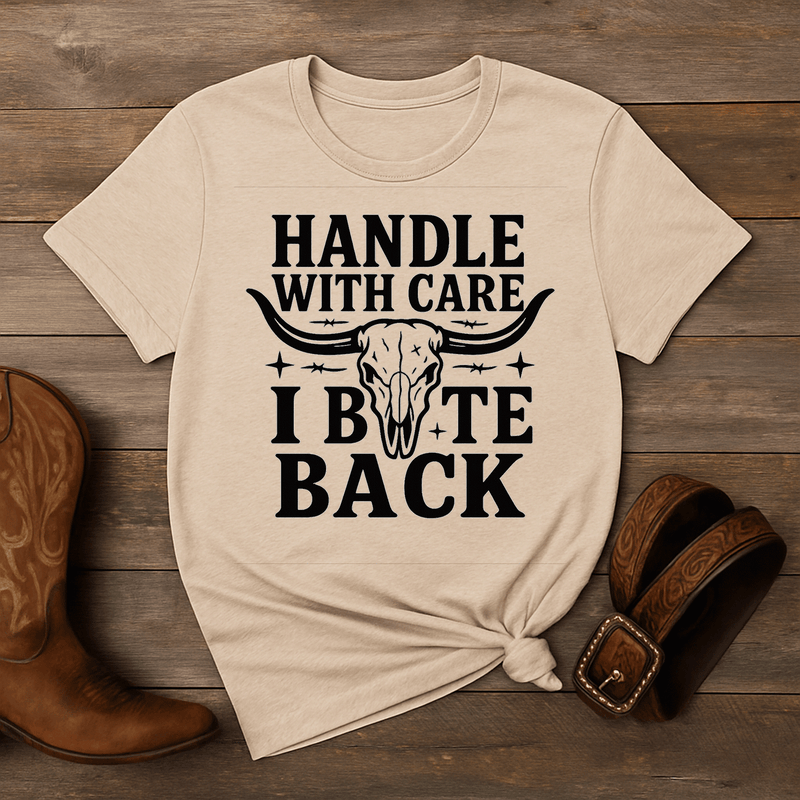 Beige t-shirt with graphic design and text on a wooden surface with boots and a belt.