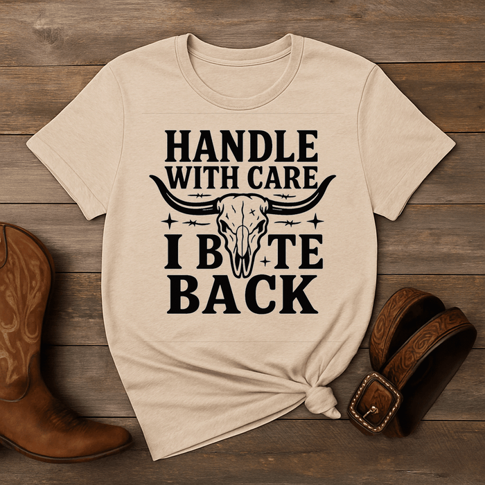 Beige t-shirt with graphic design and text on a wooden surface with boots and a belt.