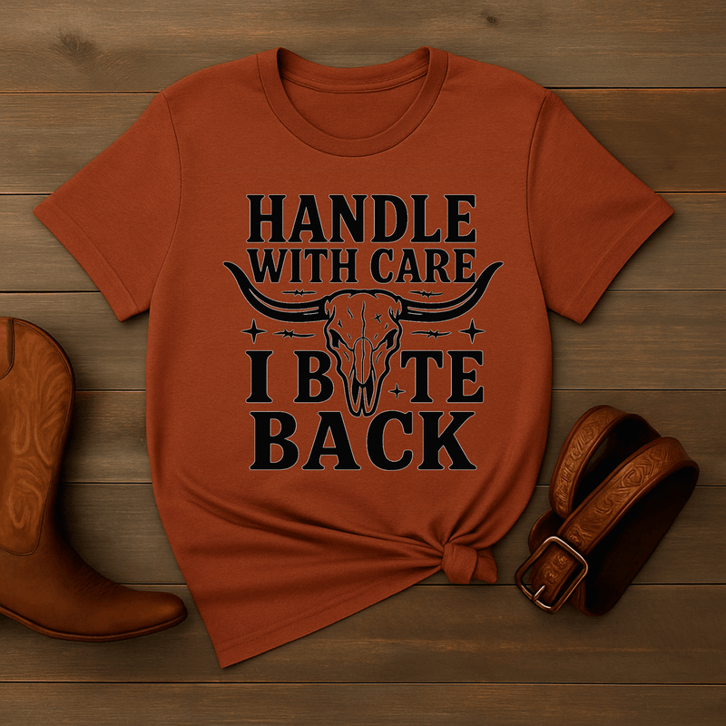 Orange t-shirt with graphic design and text on a wooden surface with cowboy boot and belt.