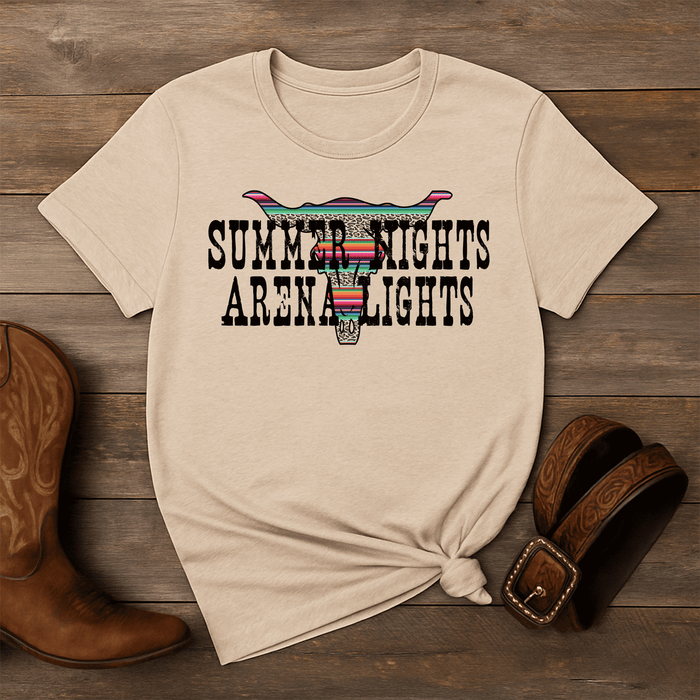 Beige t-shirt with 'Summer Nights Arena Lights' design on a wooden surface with cowboy boots and a belt.