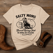 Beige t-shirt with 'Salty Moms Barrel Racing Club' graphic on a wooden surface with cowboy boots and a belt.